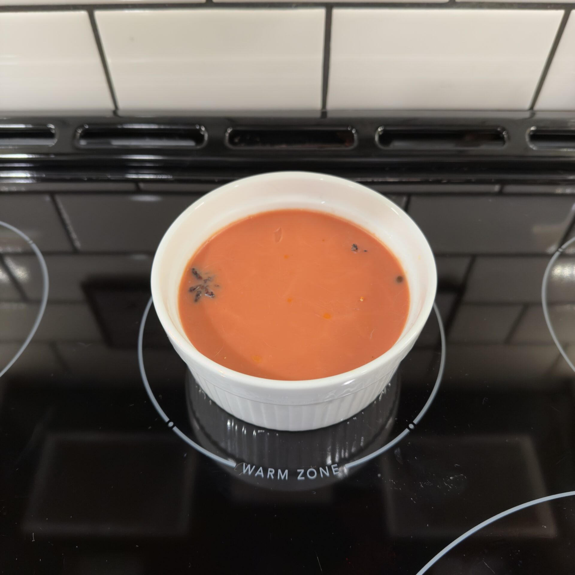 A white decorative bowl filled with creamy red colored wax on a glass stove top